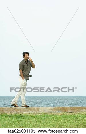 Man standing, using cell phone, body of water in background View Large Photo Image Stock Photography - Man standing, using cell phone, body of water in background. Fotosearch