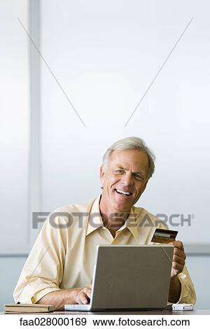 Man using laptop computer, holding credit card, smiling at camera View Large Photo Image Stock Photo - Man using laptop computer, holding credit card, smiling at camera. Fotosearch