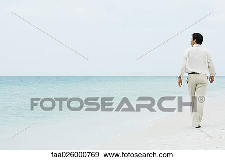 Man walking across beach, looking at distance, full length, rear view View Large Photo Image Stock Photo - Man walking across beach, looking at distance, full length, rear view. Fotosearch