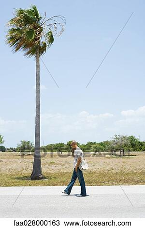 Man walking along road beside palm tree, using cell phone, side view View Large Photo Image Stock Image - Man walking along road beside palm tree, using cell phone, side view. Fotosearch