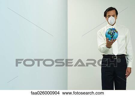 Man wearing pollution mask, holding globe, eyes closed View Large Photo Image Picture - Man wearing pollution mask, holding globe, eyes closed. Fotosearch
