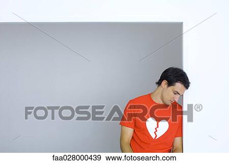 Man wearing tee-shirt with broken heart symbol, looking down View Large Photo Image Stock Photo - Man wearing tee-shirt with broken heart symbol, looking down. Fotosearch