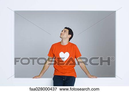 Man wearing tee-shirt with heart symbol, looking up, smiling View Large Photo Image Stock Photo - Man wearing tee-shirt with heart symbol, looking up, smiling. Fotosearch