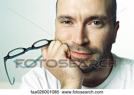Man with hand under chin, holding glasses, looking at camera, portrait View Large Photo Image Stock Photography - Man with hand under chin, holding glasses, looking at camera, portrait. Fotosearch