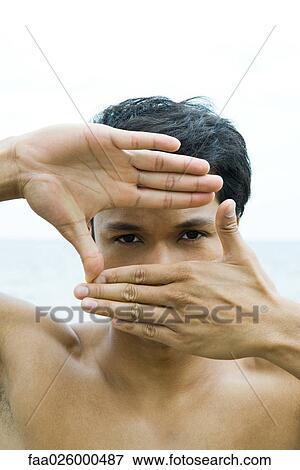 Stock Photo - Man with hands raised, looking through finger frame at camera. Fotosearch