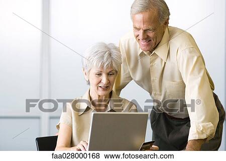 Mature couple looking at laptop computer together, smiling, woman sitting, man standing View Large Photo Image Stock Photo - Mature couple looking at laptop computer together, smiling, woman sitting, man standing. Fotosearch