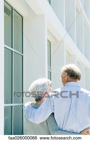 Mature couple walking with arms around each other, rear view View Large Photo Image Stock Photograph - Mature couple walking with arms around each other, rear view. Fotosearch