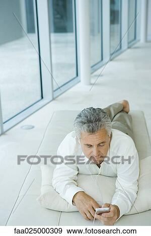 Mature man lying on chaise longue listening to mp3 player, high angle view View Large Photo Image Stock Photo - Mature man lying on chaise longue listening to mp3 player, high angle view. Fotosearch