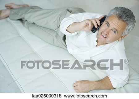 Mature man lying on chaise longue using cordless phone, looking up at camera View Large Photo Image Stock Photo - Mature man lying on chaise longue using cordless phone, looking up at camera. Fotosearch