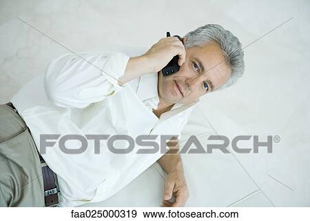 Mature man lying on side using cordless phone, looking up at camera View Large Photo Image Stock Photo - Mature man lying on side using cordless phone, looking up at camera. Fotosearch