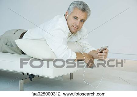 Mature man lying on stomach on chaise longue, listening to mp3 player, looking at camera View Large Photo Image Stock Image - Mature man lying on stomach on chaise longue, listening to mp3 player, looking at camera. Fotosearch