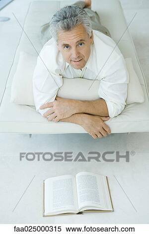 Mature man lying on stomach on chaise longue in front of book, looking up at camera View Large Photo Image Stock Photography - Mature man lying on stomach on chaise longue in front of book, looking up at camera. Fotosearch