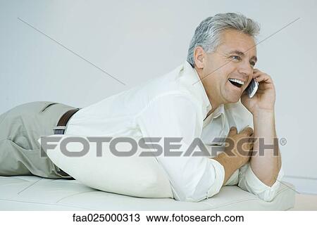 Mature man lying on stomach, using cell phone, laughing View Large Photo Image Stock Image - Mature man lying on stomach, using cell phone, laughing. Fotosearch