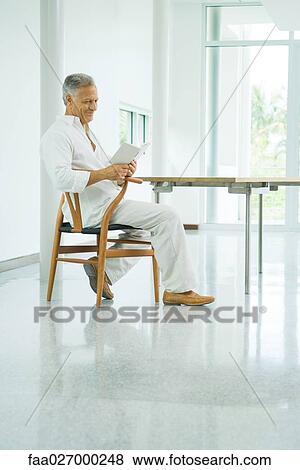 Mature man sitting at table, reading book, side view View Large Photo Image Stock Photo - Mature man sitting at table, reading book, side view. Fotosearch