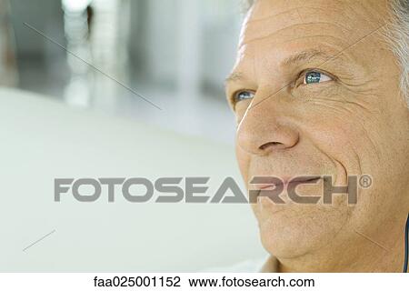 Stock Image - Mature man smiling, looking away, cropped view of face. Fotosearch