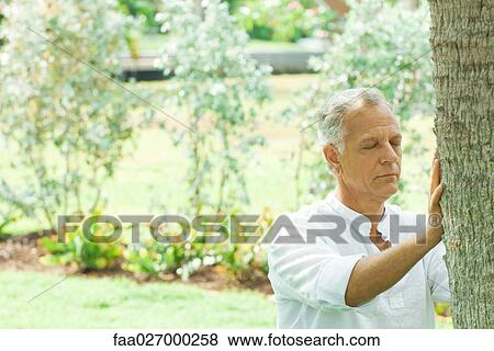 Mature man touching tree trunk, eyes closed View Large Photo Image Stock Photo - Mature man touching tree trunk, eyes closed. Fotosearch