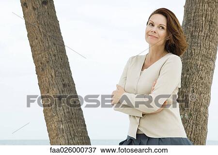 Mature woman leaning against palm tree, smiling View Large Photo Image Stock Photo - Mature woman leaning against palm tree, smiling. Fotosearch