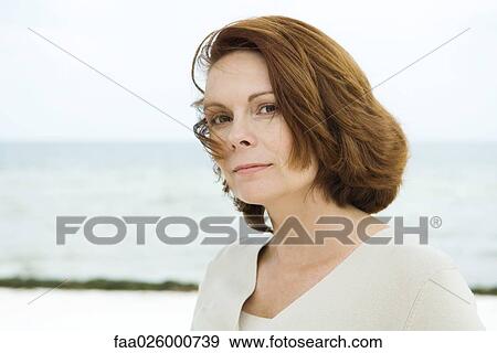 Stock Photo - Mature woman, looking at camera, sea in background. Fotosearch