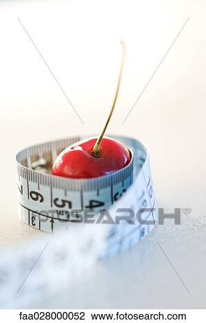 Stock Image - Measuring tape wrapped around cherry, close-up. Fotosearch