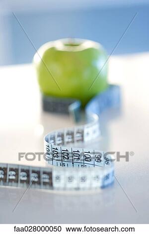 Stock Image - Measuring tape wrapped around green apple, close-up. Fotosearch