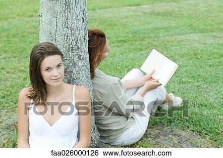 Mother and daughter leaning against tree trunk, woman reading book, teen girl smiling at camera View Large Photo Image Stock Photograph - Mother and daughter leaning against tree trunk, woman reading book, teen girl smiling at camera. Fotosearch