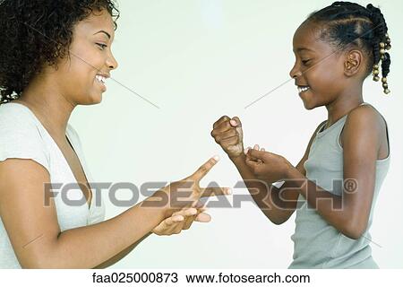 Stock Image - Mother and daughter playing rock paper scissors, side view. Fotosearch