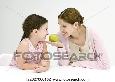 Mother and daughter sitting face to face, smiling at each other, woman holding apple View Large Photo Image Stock Image - Mother and daughter sitting face to face, smiling at each other, woman holding apple. Fotosearch