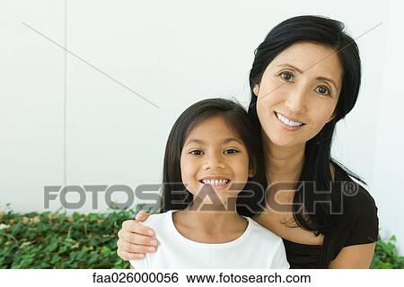 Stock Photograph - Mother and daughter smiling at camera together, portrait. Fotosearch