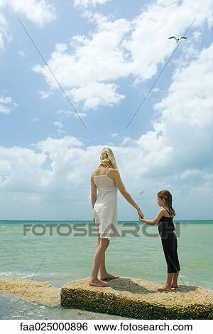 Mother and daughter standing on breakwater, holding hands, facing ocean View Large Photo Image Stock Photograph - Mother and daughter standing on breakwater, holding hands, facing ocean. Fotosearch