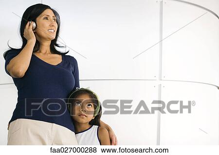 Stock Photo - Mother and daughter standing side by side, listening to headphones. Fotosearch