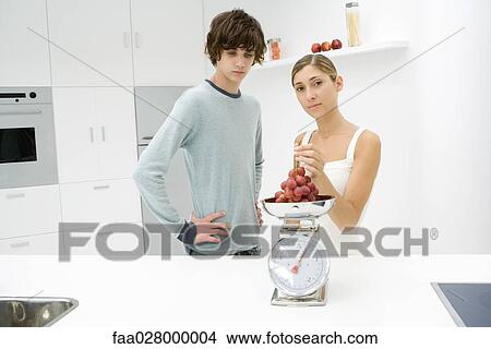 Mother and son standing in kitchen, weighing grapes on scale, woman looking at camera View Large Photo Image Picture - Mother and son standing in kitchen, weighing grapes on scale, woman looking at camera. Fotosearch