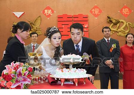 Newlyweds blowing out candle on wedding cake together View Large Photo Image Stock Photo - Newlyweds blowing out candle on wedding cake together. Fotosearch