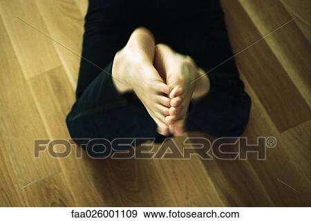 Stock Photo - Person lying on floor, bare feet raised, cropped view. Fotosearch