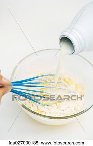 Stock Photography - Person pouring milk into mixing bowl, holding whisk, cropped view. Fotosearch