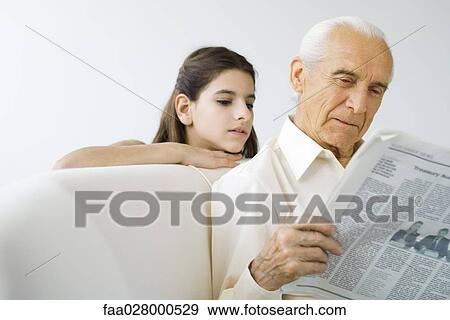 Stock Photo - Preteen girl looking over grandfather's shoulder while he reads newspaper. Fotosearch