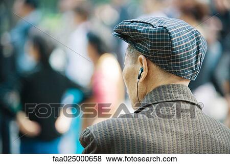 Stock Photo - Senior man listening to earphones, rear view, head and shoulders. Fotosearch