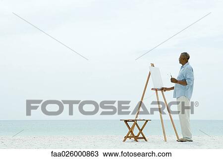 Senior man standing in front of blank canvas at the beach, holding paint brushes View Large Photo Image Stock Image - Senior man standing in front of blank canvas at the beach, holding paint brushes. Fotosearch