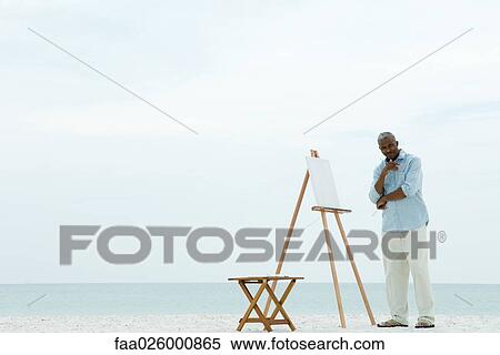 Senior man standing next to blank canvas at the beach, holding paint brushes, smiling at camera View Large Photo Image Stock Photography - Senior man standing next to blank canvas at the beach, holding paint brushes, smiling at camera. Fotosearch