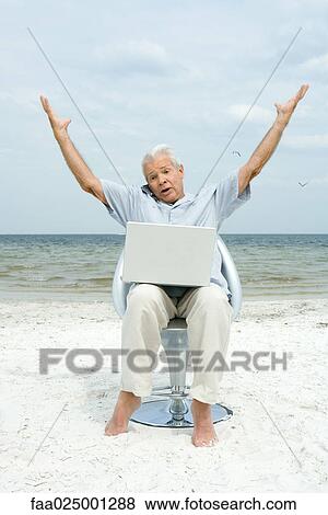 Senior man using laptop and cell phone on beach, raising arms View Large Photo Image Stock Photo - Senior man using laptop and cell phone on beach, raising arms. Fotosearch