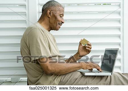 Stock Photography - Senior man using laptop, making on-line purchase with credit card. Fotosearch