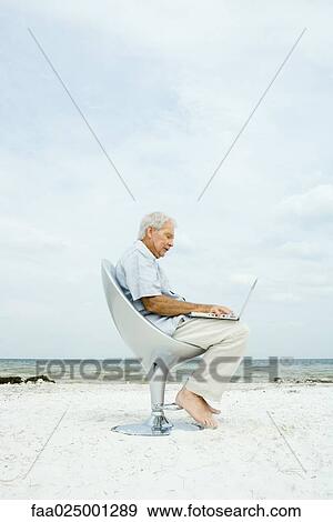 Senior man using laptop on beach, side view View Large Photo Image Stock Photo - Senior man using laptop on beach, side view. Fotosearch