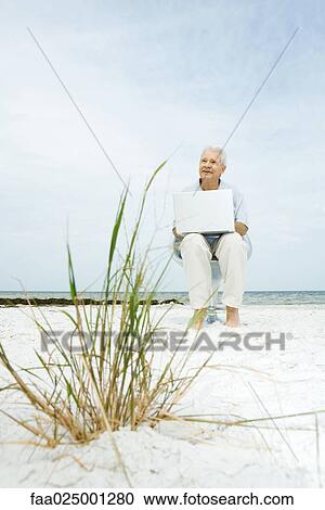 Senior man using laptop on beach View Large Photo Image Stock Image - Senior man using laptop on beach. Fotosearch