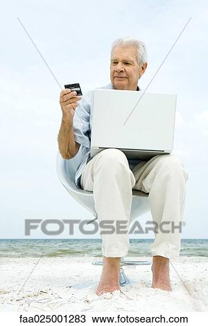 Senior man using laptop on beach, making on-line purchase with credit card View Large Photo Image Stock Image - Senior man using laptop on beach, making on-line purchase with credit card. Fotosearch