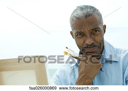 Senior man with hand under chin, holding paint brushes, smiling at camera View Large Photo Image Stock Photo - Senior man with hand under chin, holding paint brushes, smiling at camera. Fotosearch