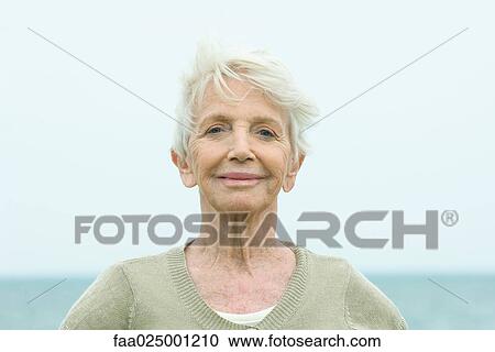 Stock Image - Senior woman smiling at camera, ocean horizon in background, portrait. Fotosearch