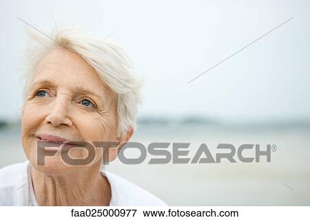 Senior woman smiling, looking up, beach in background View Large Photo Image Stock Photo - Senior woman smiling, looking up, beach in background. Fotosearch