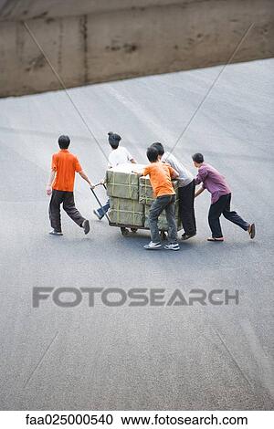 Stock Image - Small group pulling packages on cart, high angle view. Fotosearch