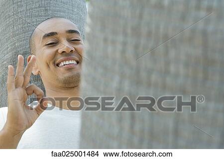 smiling, tree trunk, hand raised, ok sign, raising eyebrows, toothy smile View Large Photo Image Picture - smiling, tree trunk, hand raised, ok sign, raising eyebrows, toothy smile. Fotosearch