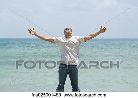 Stock Photo - standing, head back, arms out, arms outstretched, water's edge, mid adult men. Fotosearch