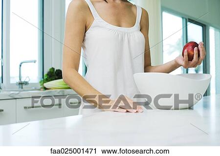 Stock Image - standing, woman, apple, bowl, holding, behind, kitchen counter. Fotosearch